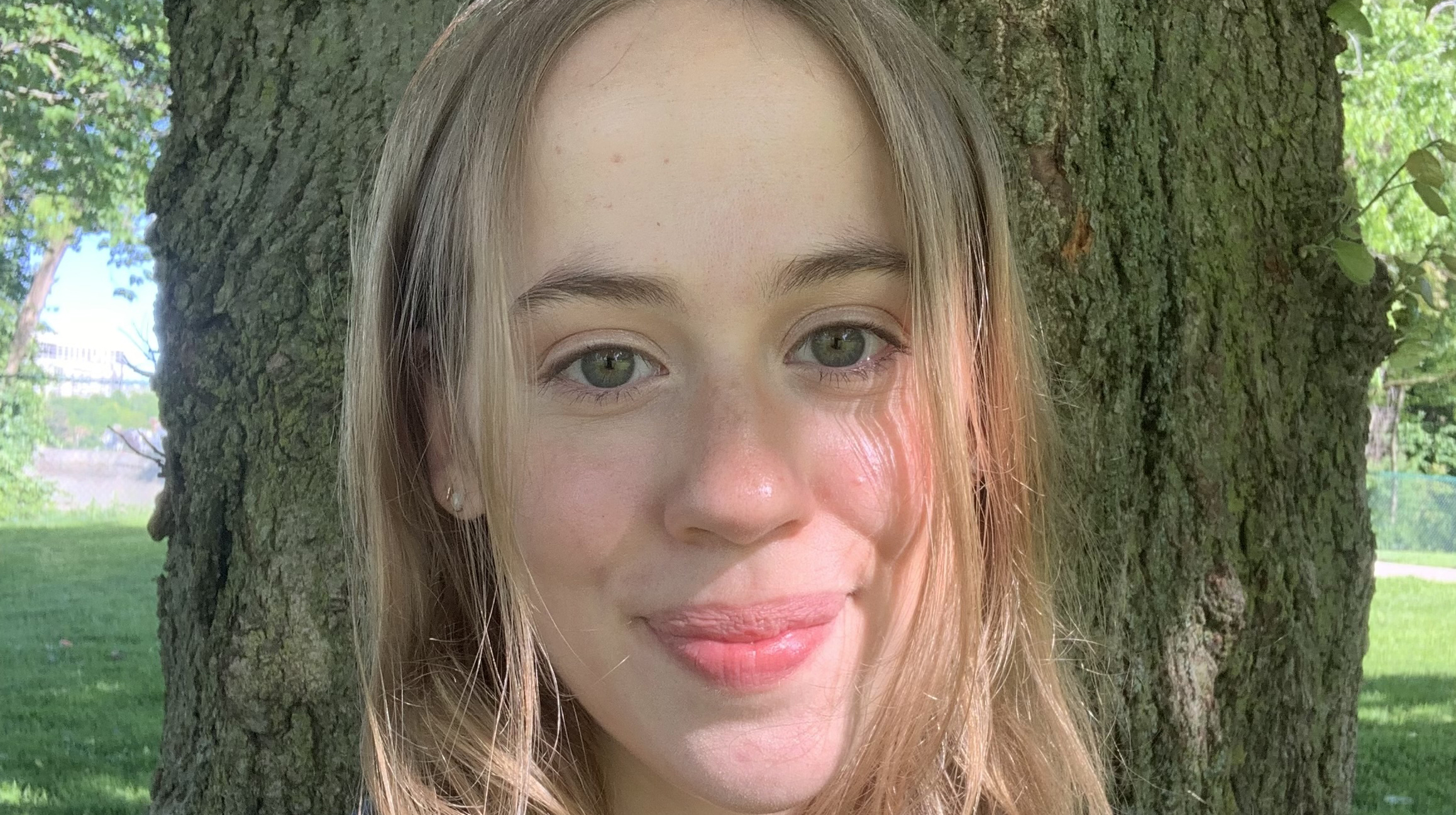 Close-up of a young girl smiling outdoors in front of a tree